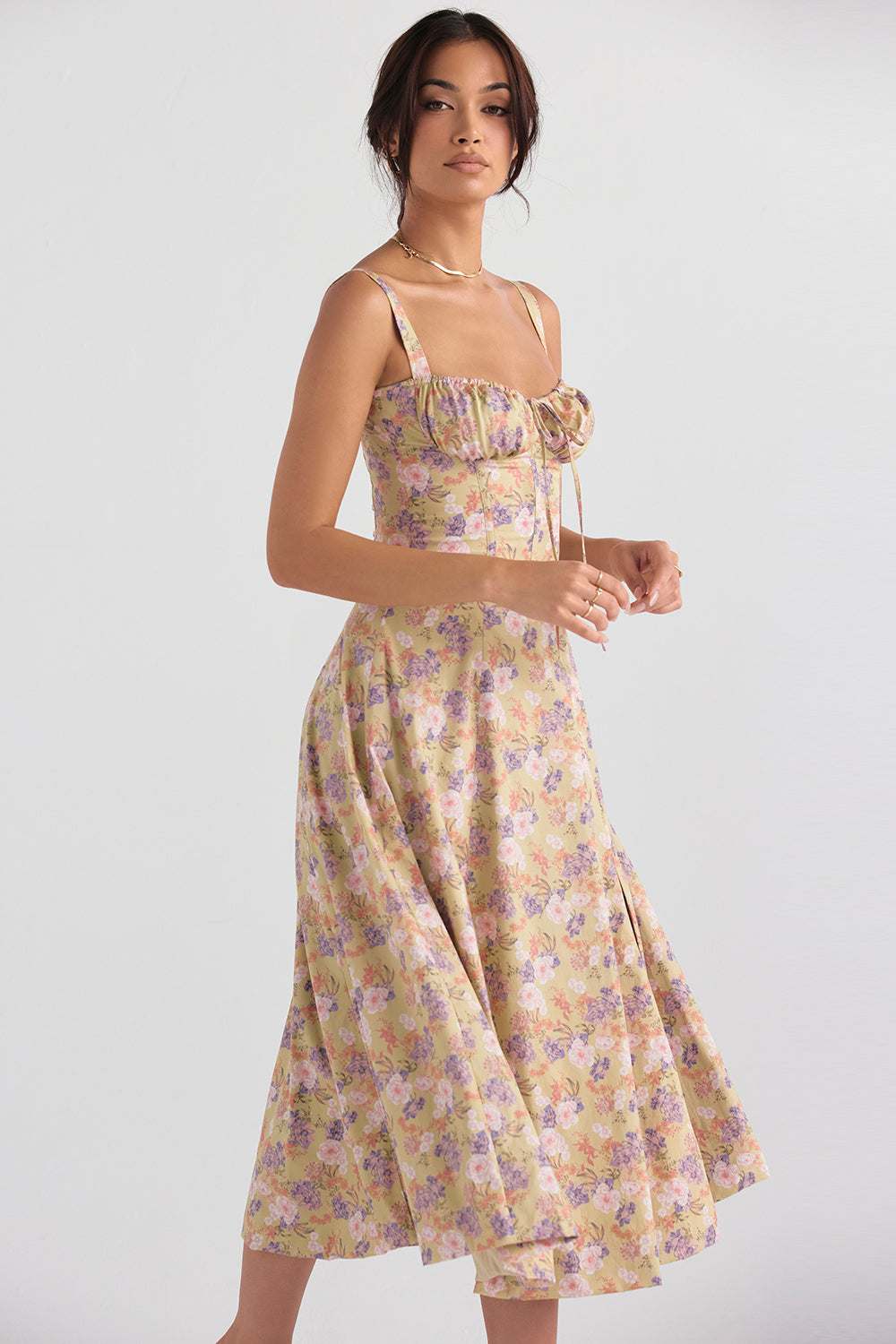 Kvinde iført blomsterprintet sommerkjole i pastelfarver, poserer mod hvid baggrund. Elegant design, perfekt til forår og sommermode.