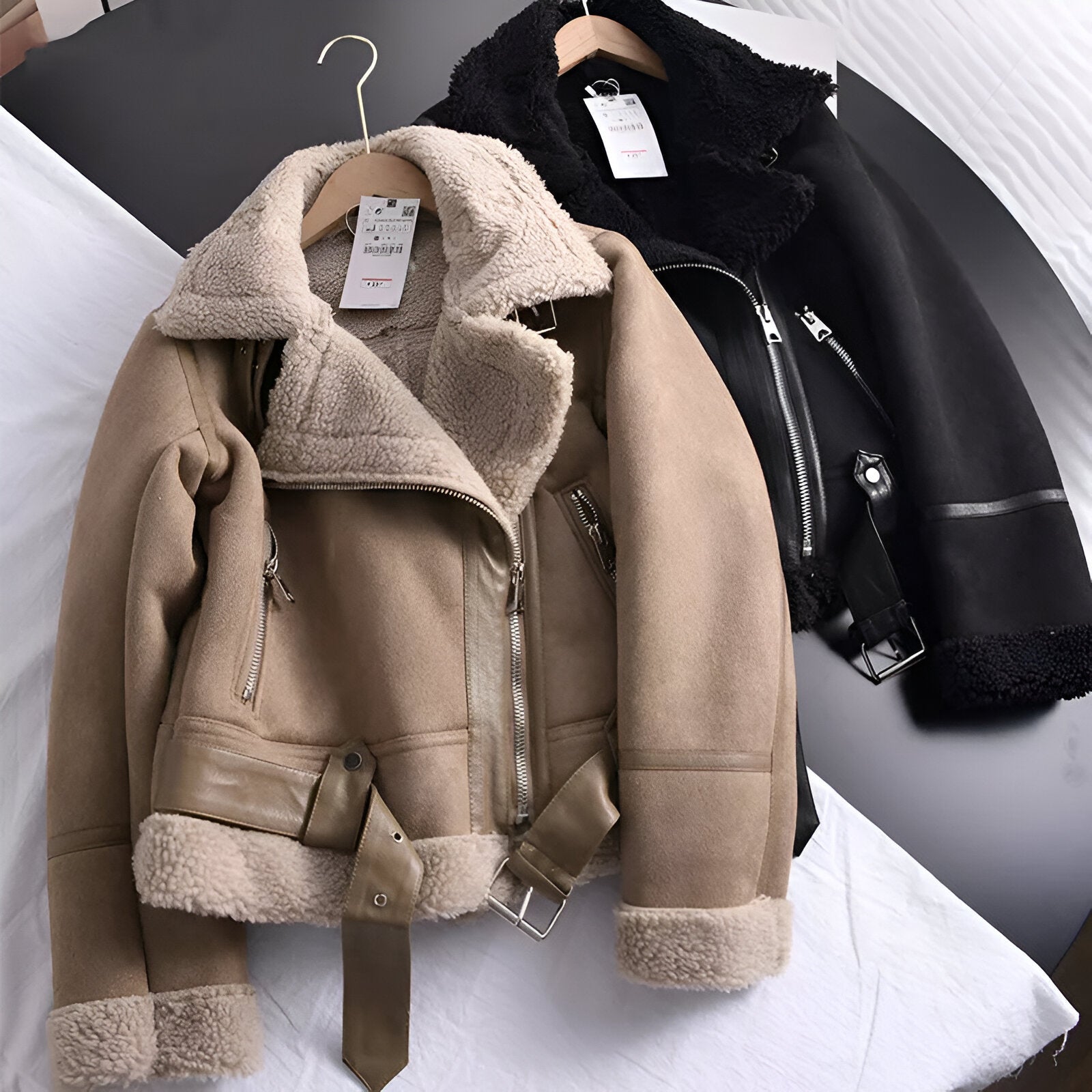 To læderjakker med pelsfor, en i beige og en i sort, hænger på bøjler. Perfekt til vintermode, stilfuldt design med lynlåse og bælter.