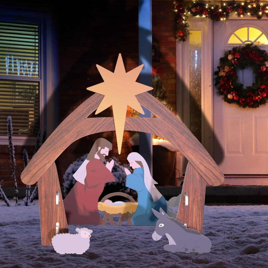 Julekrybbe med Jesusbarnet, Maria, Josef, får og æsel foran sneklædt hus med julepynt. Stjerne over krybben. Julestemning udendørs.