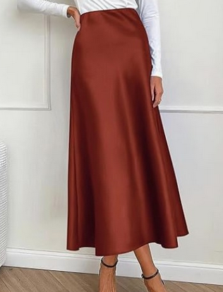 Kvinde iført lang brun satin nederdel og hvid bluse, står på trægulv. Elegant mode, stilfuldt tøj, moderne kvindemode, minimalistisk design.