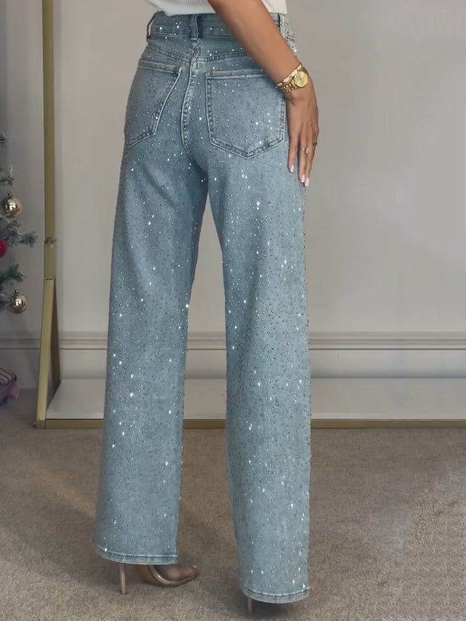 Kvinde iført glitrende blå jeans med høj talje og brede ben, stående på tæppe. Perfekt til mode, stil og trendy tøj.
