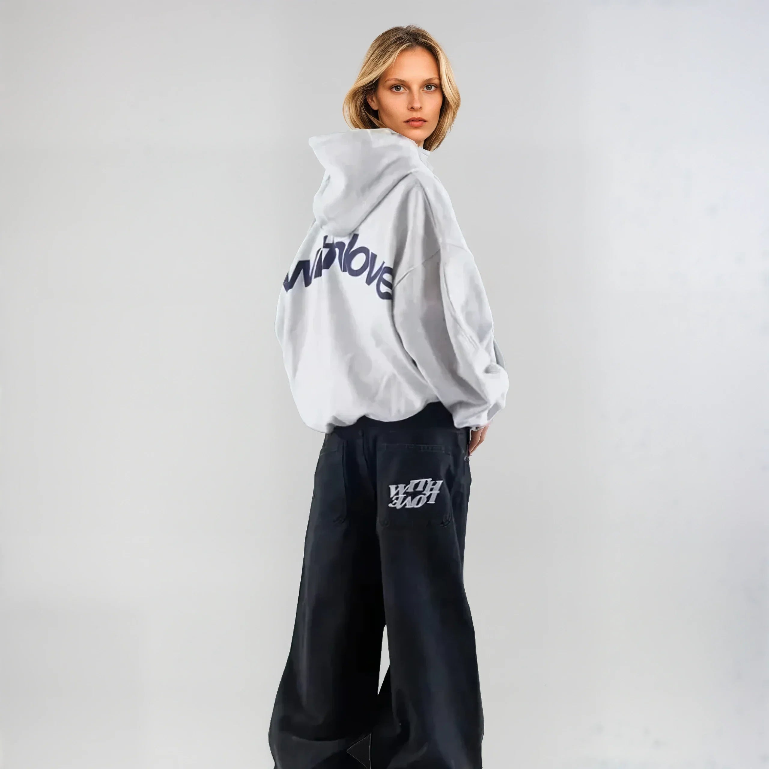 Kvinde iført hvid hættetrøje med "WINDLOVE" tekst og sorte bukser med "WITH LOVE" logo. Moderne streetwear mode, afslappet stil.