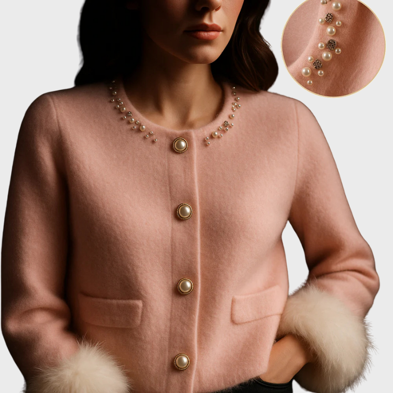 Kvinde iført lyserød uldjakke med perleknapper og pelsmanchetter. Fokus på perledekoration ved halsudskæring. Elegant og stilfuldt design.