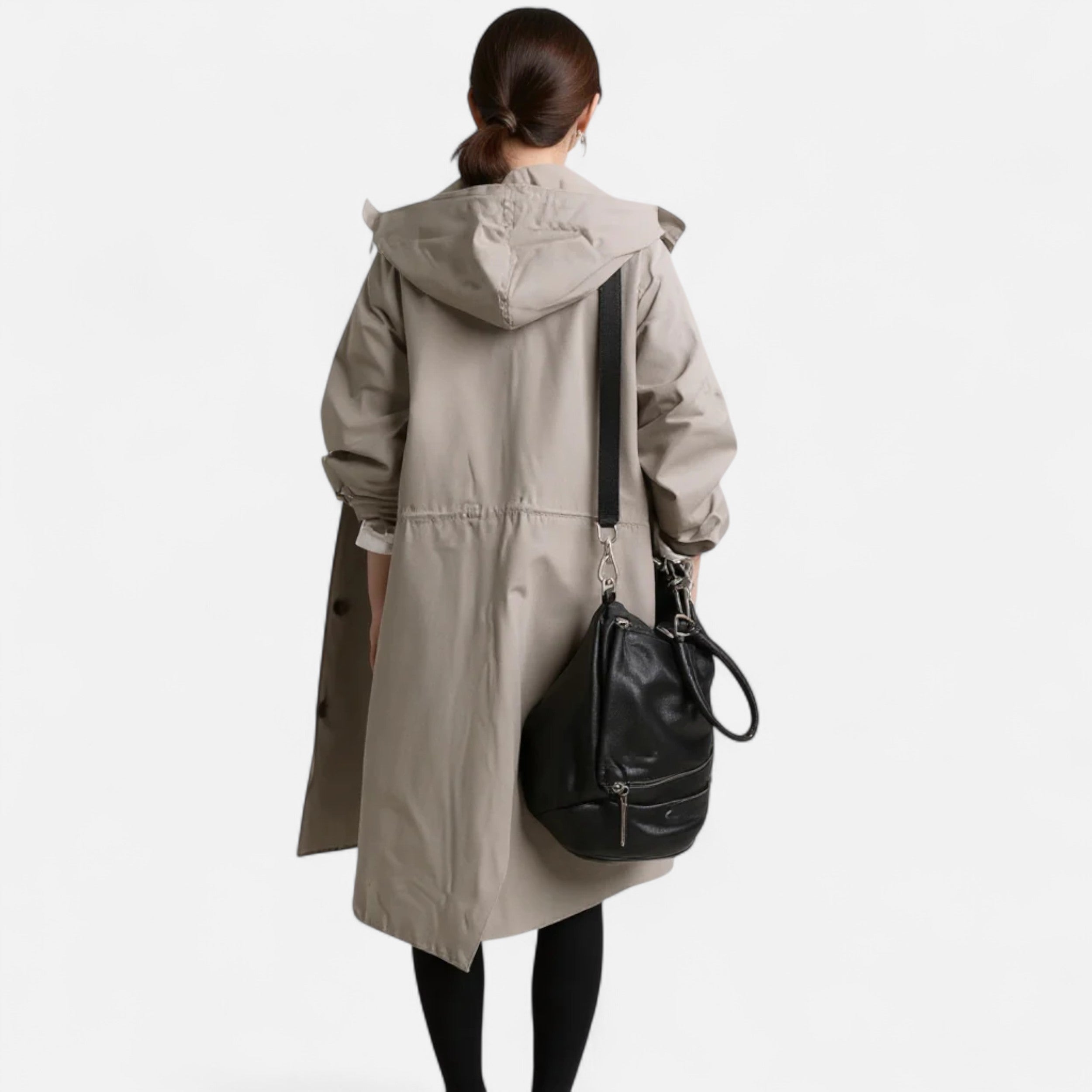 Kvinde i beige trenchcoat set bagfra, bærer sort lædertaske. Stilfuldt efterårsoutfit, moderigtigt overtøj, praktisk og elegant design.