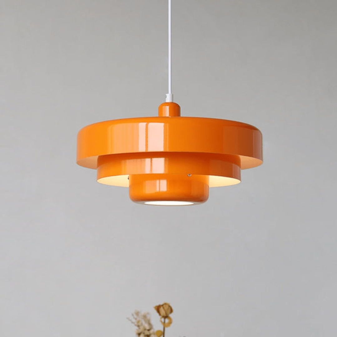 Orange retro loftlampe i metal med moderne design, hængende fra hvid ledning mod grå baggrund. Perfekt til stilfuld indretning og belysning.