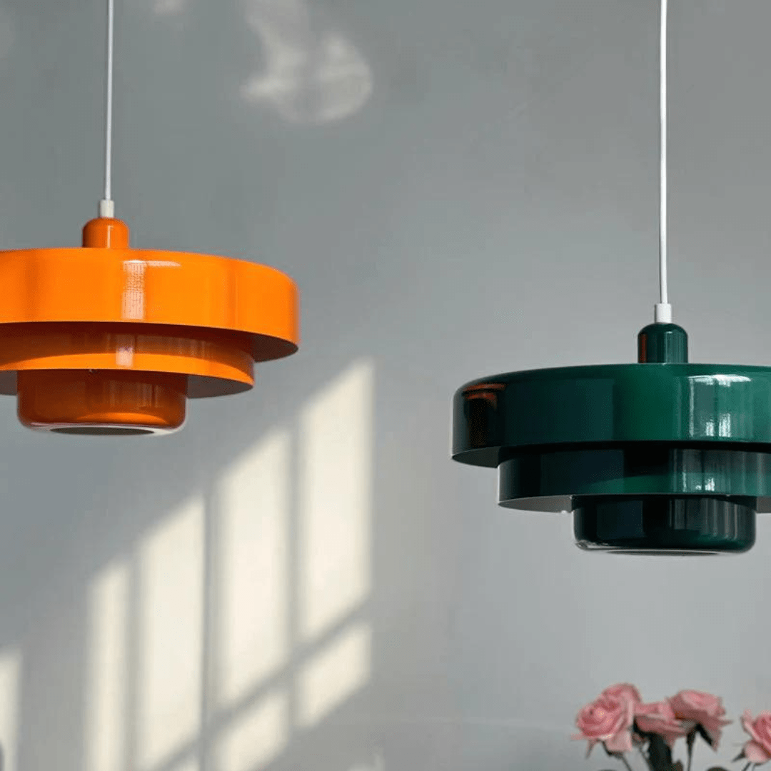 To moderne pendellamper i orange og grøn hænger fra loftet. Designet er stilrent og minimalistisk, perfekt til skandinavisk indretning.