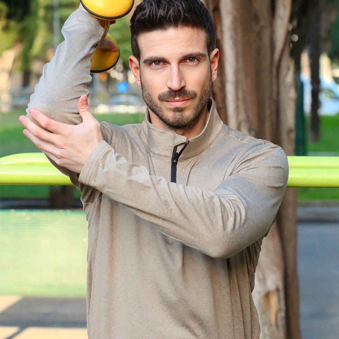 Mand træner med håndvægt i park, iført beige trøje. Fitness, udendørs træning, sund livsstil. Fokus på styrketræning og velvære.