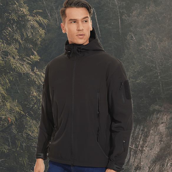 Ung mand iført sort softshell-jakke i skovmiljø, ideel til udendørsaktiviteter. Vindtæt, vandafvisende jakke til mænd, perfekt til vandreture.