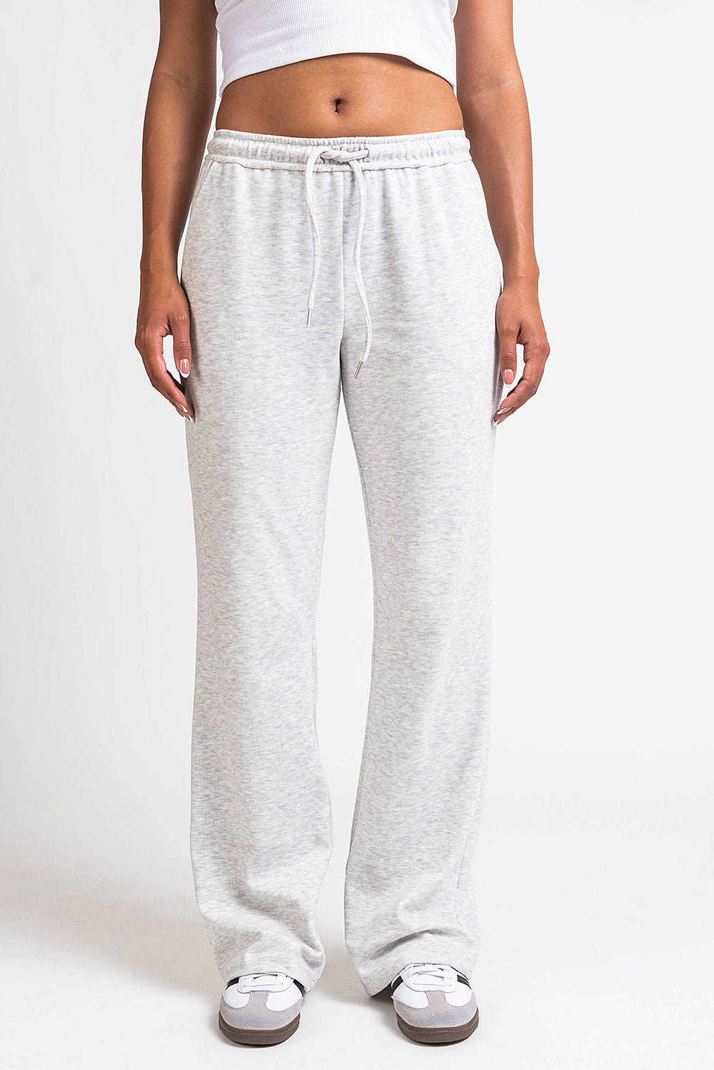 Kvinde iført grå sweatpants og hvid crop top. Komfortabelt loungewear, afslappet stil, perfekt til hjemmet eller afslappede udendørsaktiviteter.