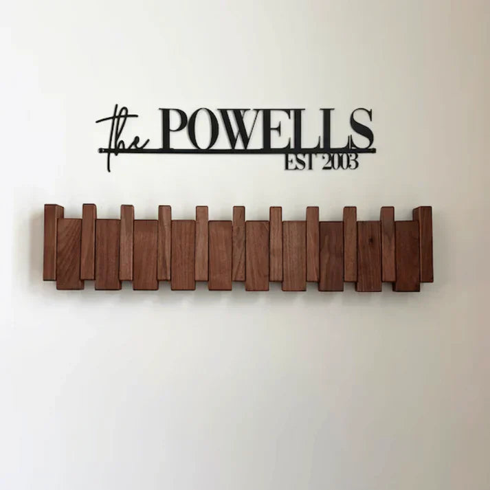 Træknagerække på væg med sort skilt "The Powells EST 2003". Moderne indretning, minimalistisk design, praktisk opbevaring.