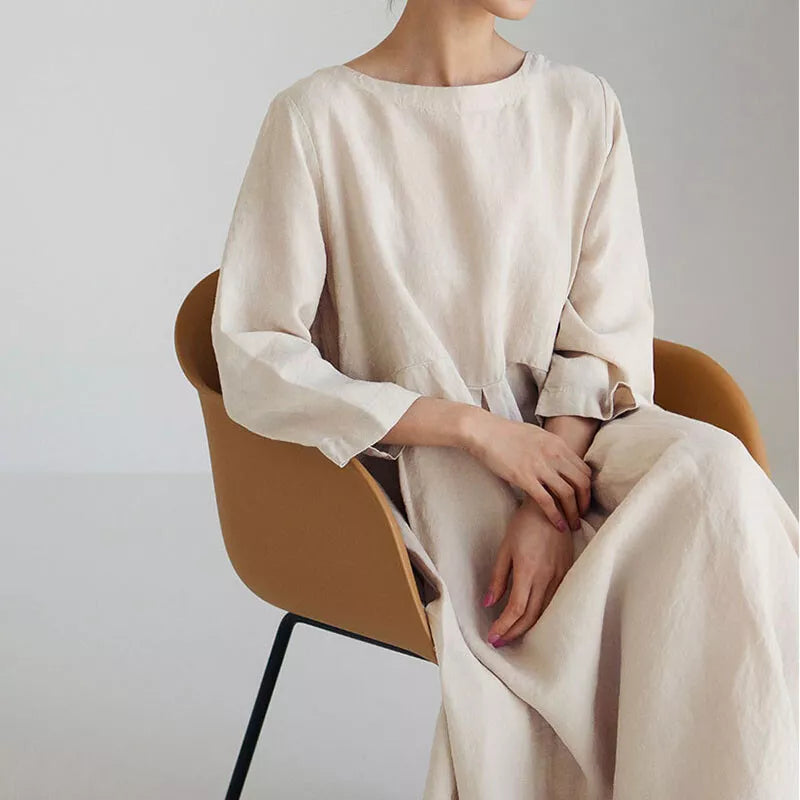 Kvinde i minimalistisk beige kjole sidder på moderne brun stol, skandinavisk design, stilfuld indretning, enkel elegance, modefotografi.