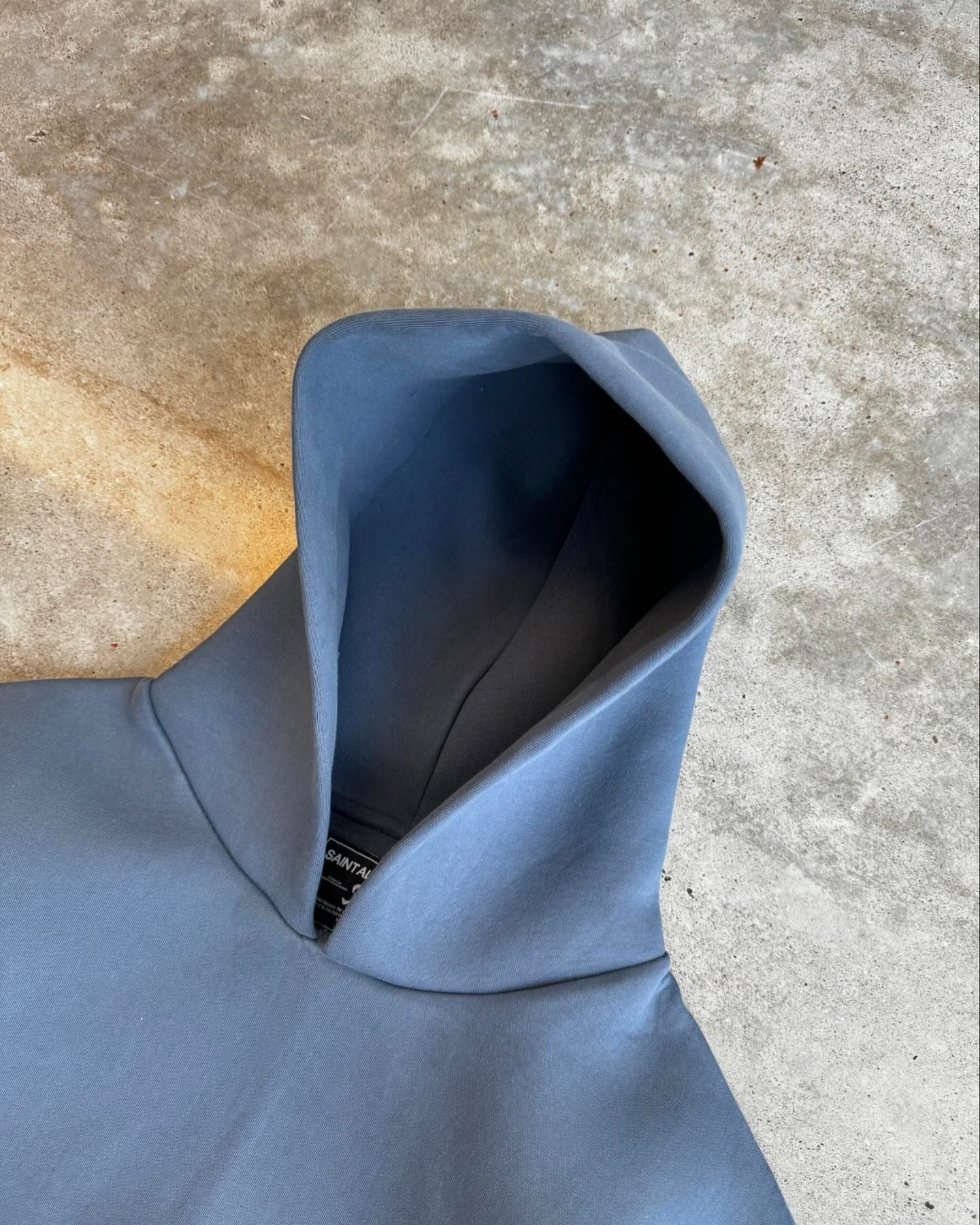 Grå hættetrøje på betonbaggrund, minimalistisk design, moderne streetwear, unisex mode, komfortabel og stilfuld beklædning.