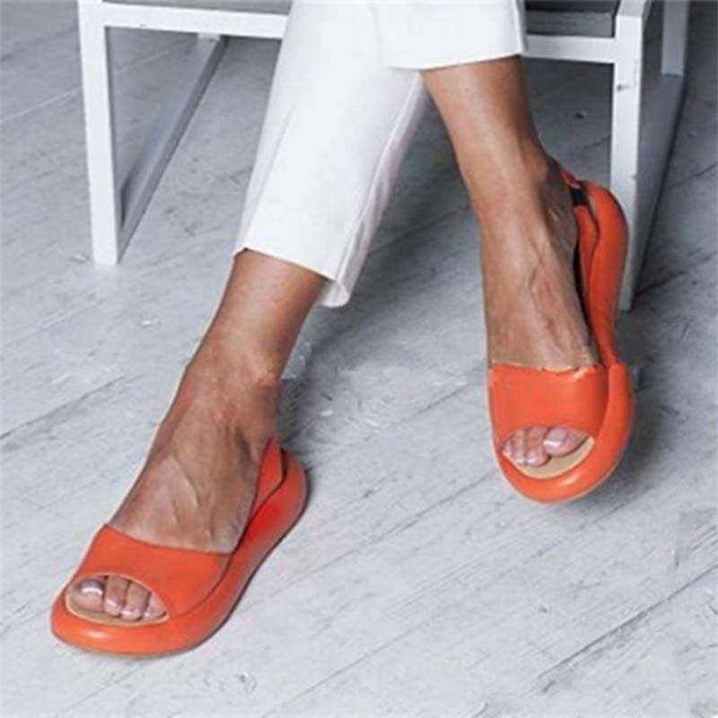 Kvinde iført orange sandaler med åben tå, sidder på hvid stol. Moderne damesko, komfortabelt design, perfekt til sommermode.