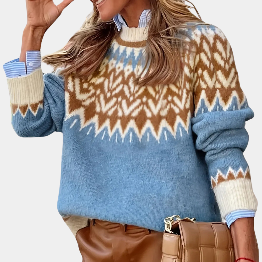 Kvinde iført blå og brun striktrøje med nordisk mønster, stribet skjorte, brune bukser og en flettet taske. Mode, vintertøj, stilfuldt look.