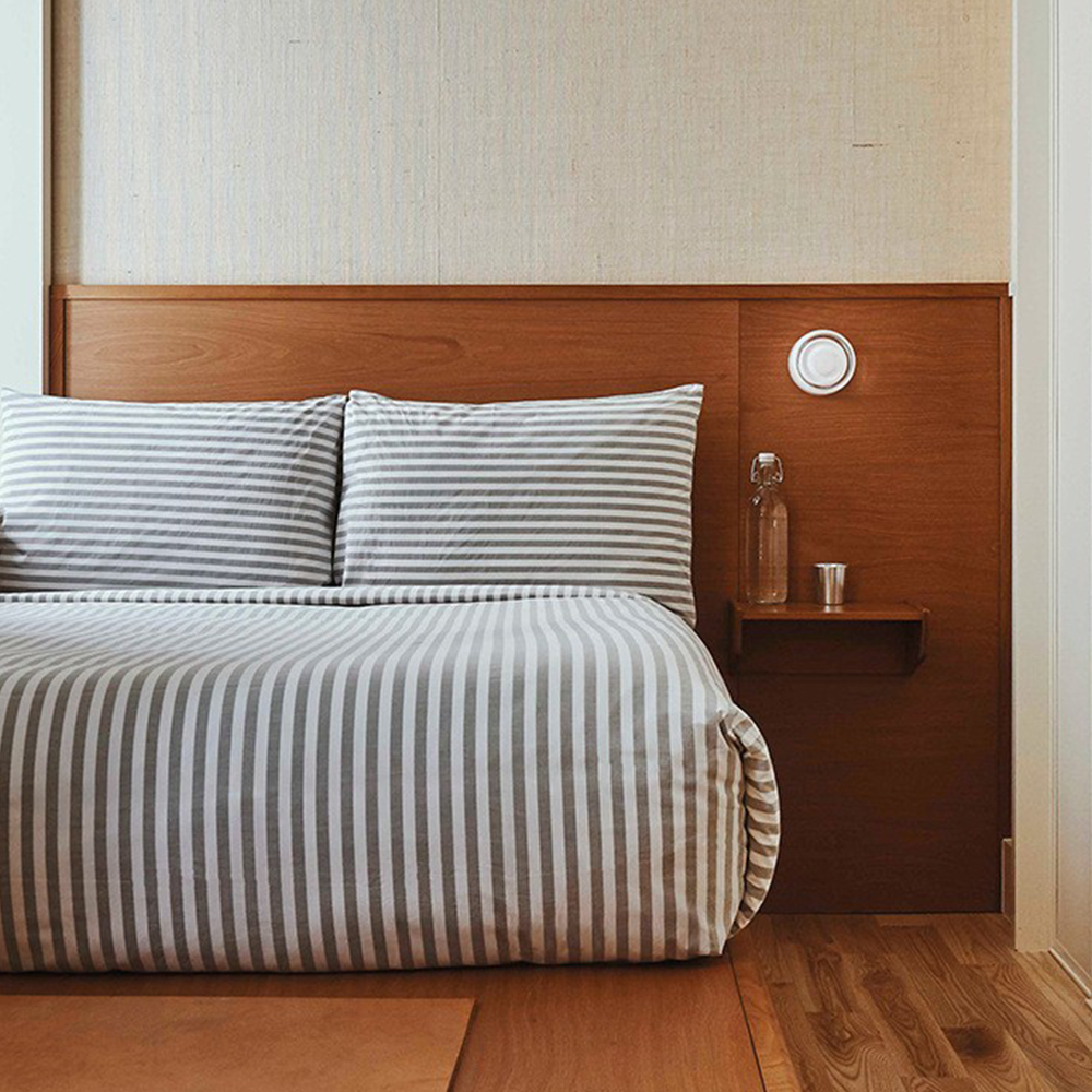 Soveværelse med stribet sengetøj, træpaneler, glasflaske og kop på hylde. Moderne indretning, minimalistisk design, komfortabel seng.