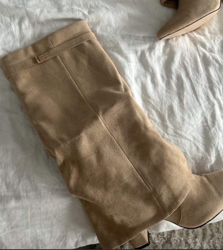 Beige knæhøje støvler i ruskind på hvidt sengetøj. Trendy fodtøj til efterår og vinter. Mode til kvinder, stilfulde støvler til hverdagsbrug.