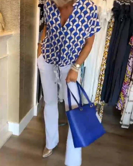 Kvinde i blå-hvid mønstret bluse og hvide bukser, holder en blå taske. Modebutik baggrund med hængende tøj. Trendy sommeroutfit.