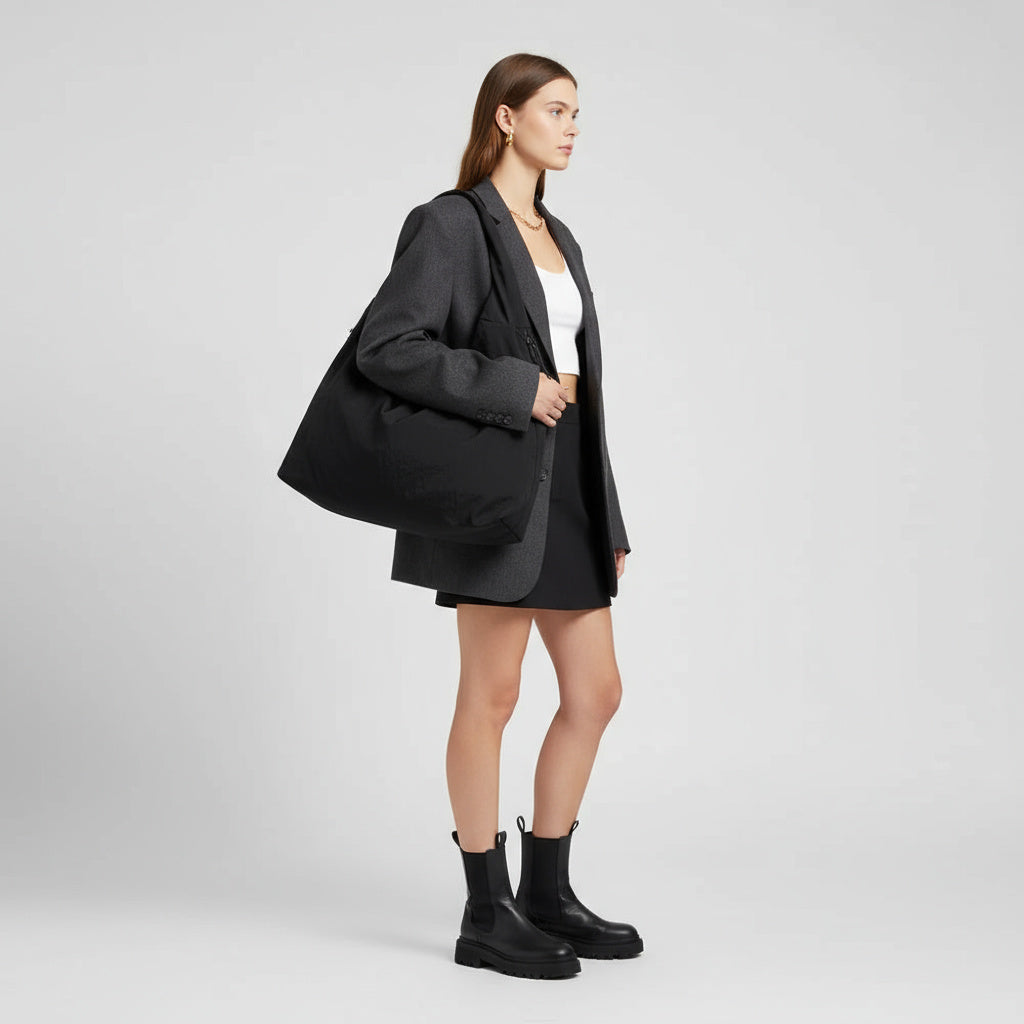 Kvinde i gråt jakkesæt med stor sort taske, hvid top og sorte støvler. Moderne mode, minimalistisk stil, elegant outfit til hverdag.