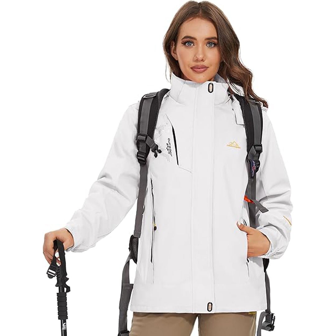 Kvinde iført hvid vandrejakke med rygsæk og vandrestav. Udendørsbeklædning, trekkingudstyr, funktionel jakke til vandring og friluftsliv.