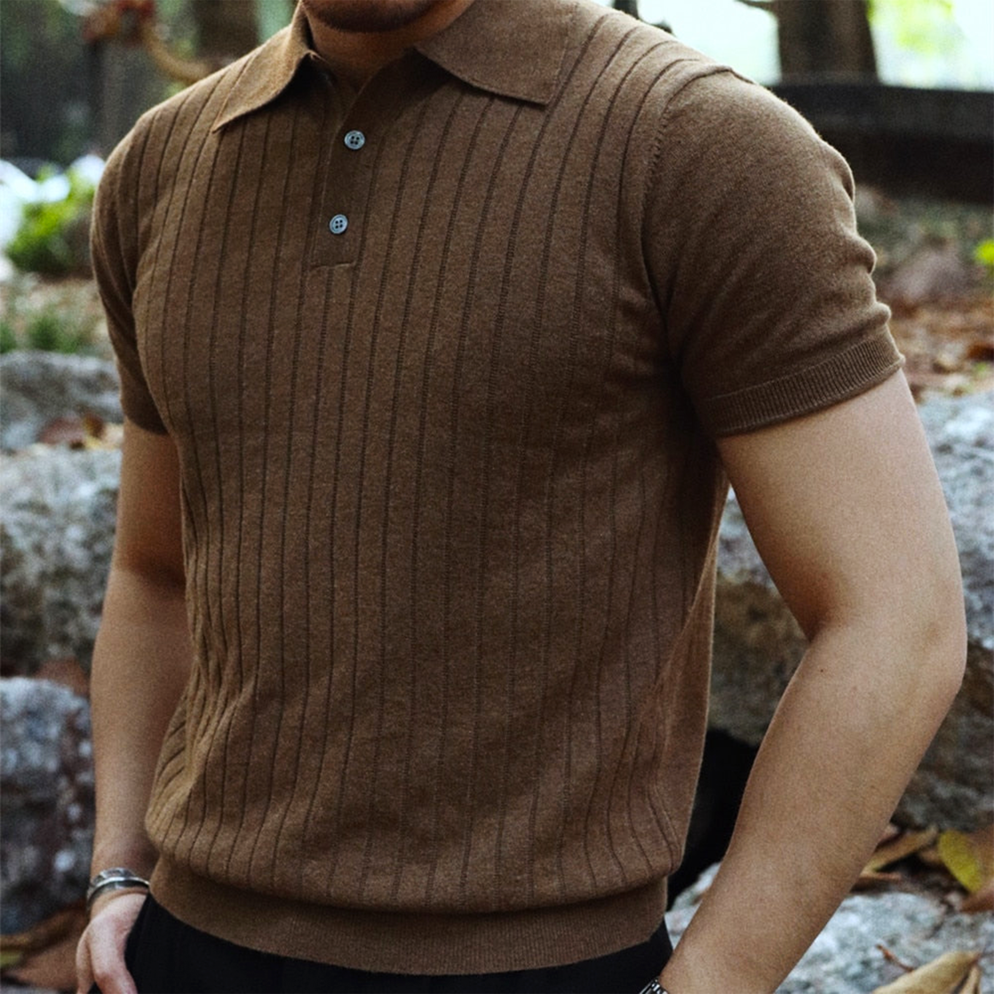Brun striktrøje med korte ærmer og knapper, bæres af en mand i udendørs omgivelser. Moderne herremode, efterårsbeklædning, stilfuld polo.