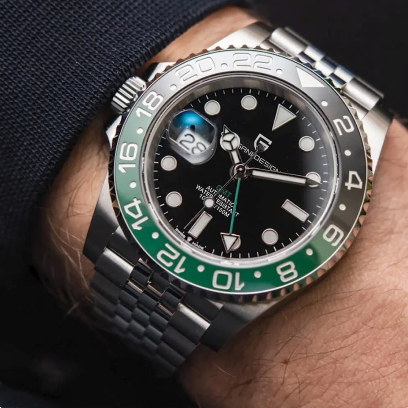 Mand iført en luksus herreur med sort urskive, grøn og sølvfarvet bezel, og dato funktion. Stilfuldt design, præcision, elegance, moderne herreur.