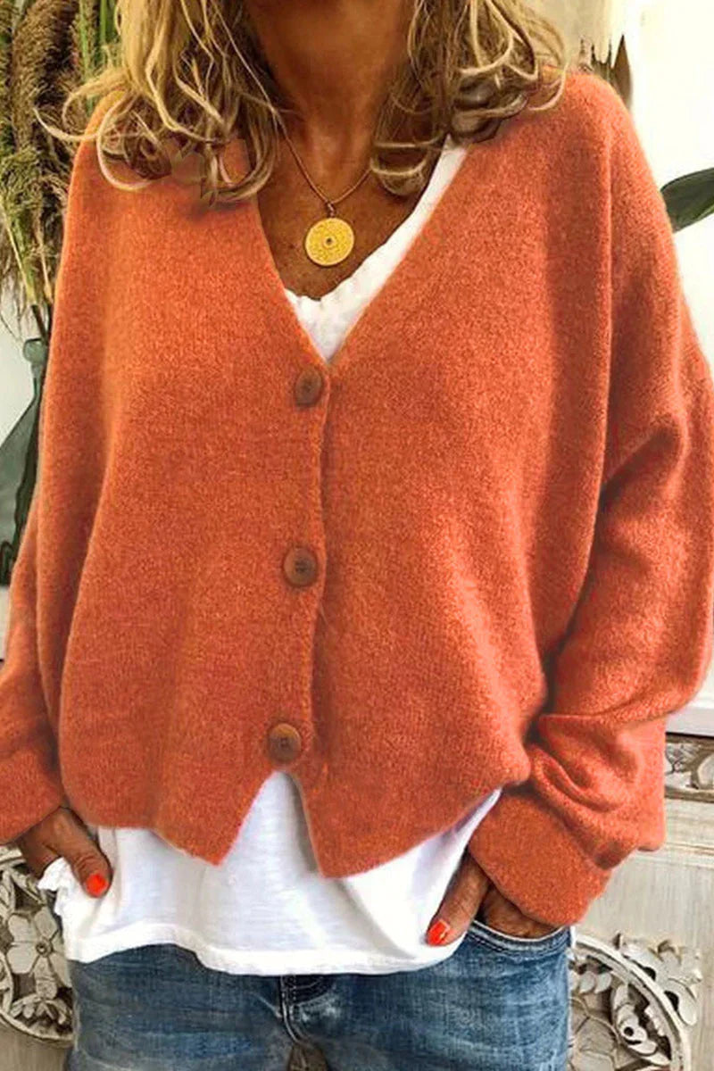 Kvinde iført orange cardigan med knapper, hvid t-shirt og jeans. Mode, efterårstøj, casual stil, komfortabelt look.