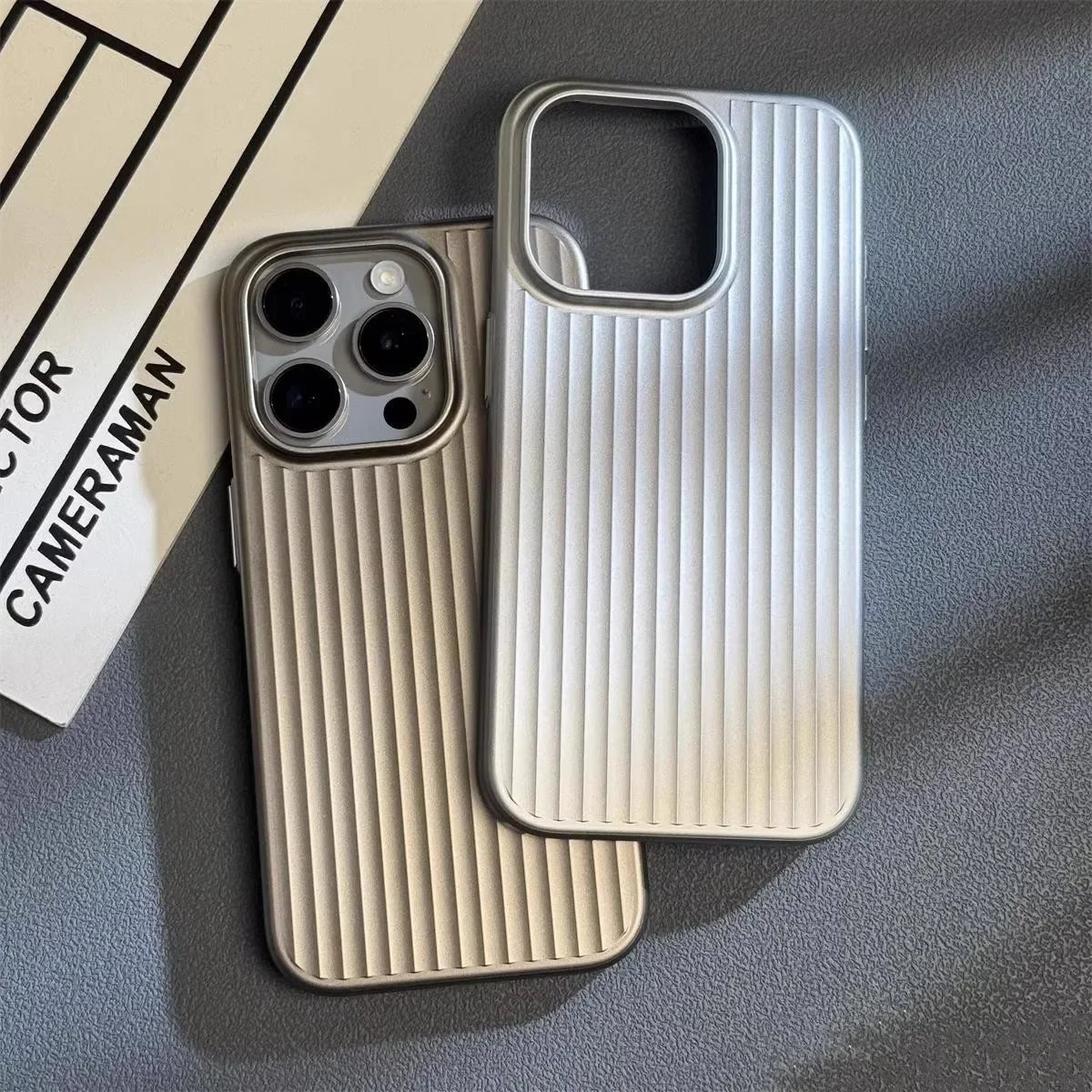 Sølvfarvet iPhone med ribbet cover og matchende tomt cover på grå overflade. Moderne smartphone tilbehør, stilfuldt design, beskyttende etui.