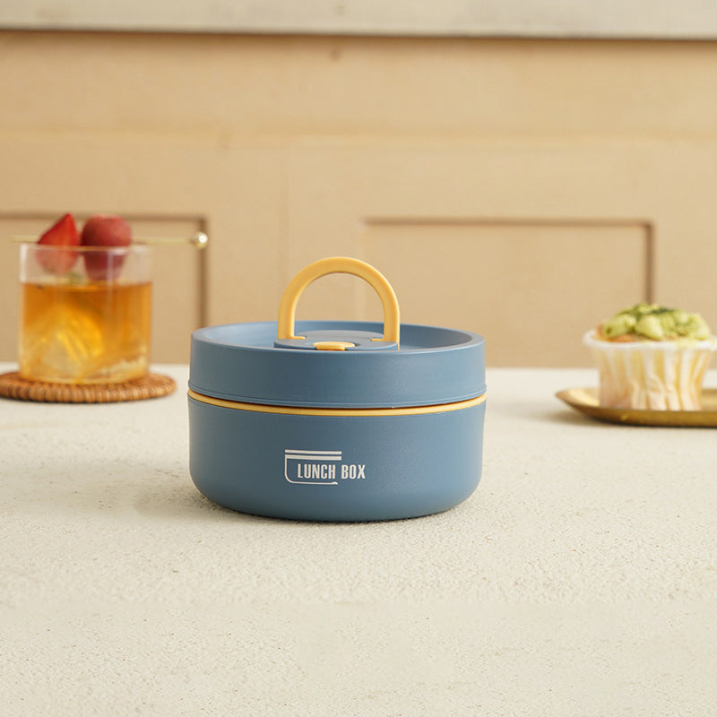 Blå madkasse med gult håndtag på bord, ved siden af glas med drik og dessert. Praktisk opbevaring til frokost. Ideel til skole og arbejde.