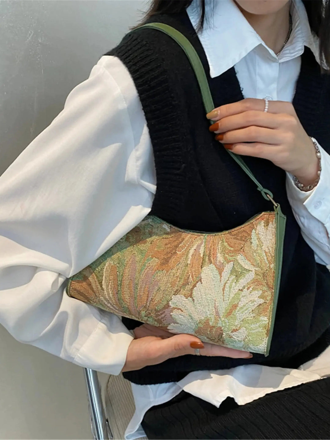 Kvinde med sort vest og hvid skjorte holder en broderet skuldertaske med blomstermønster. Elegant mode, tilbehør, trendy håndtaske.