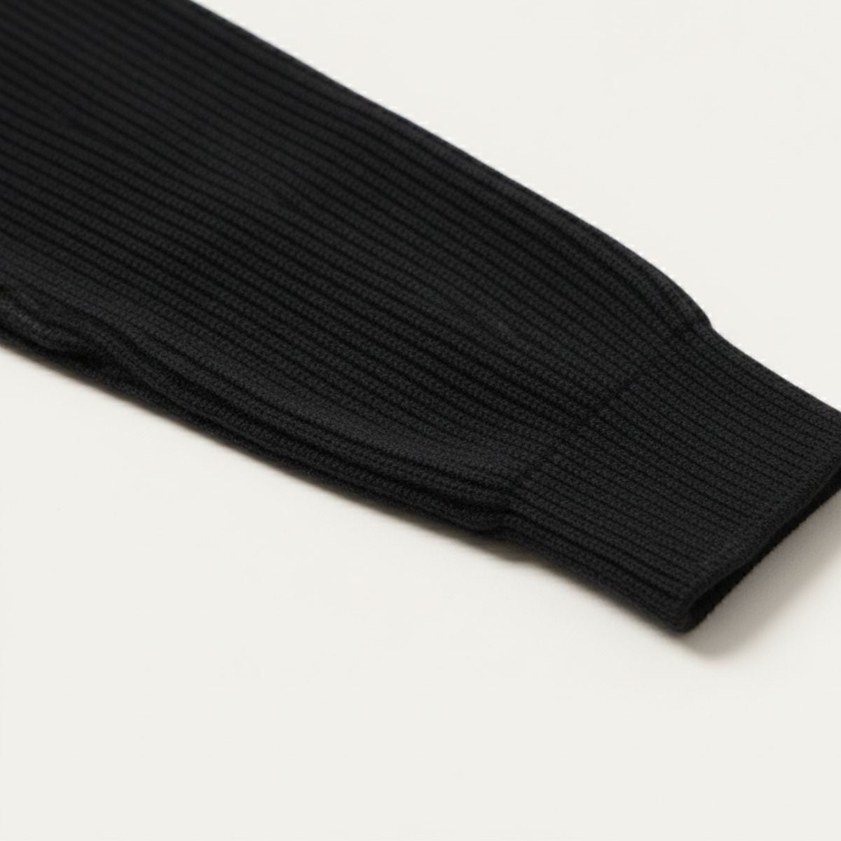 Sort ribstrikket ærme på hvid baggrund, tæt på. Moderne strikmode, minimalistisk design, høj kvalitet. Perfekt til efterår og vinter.