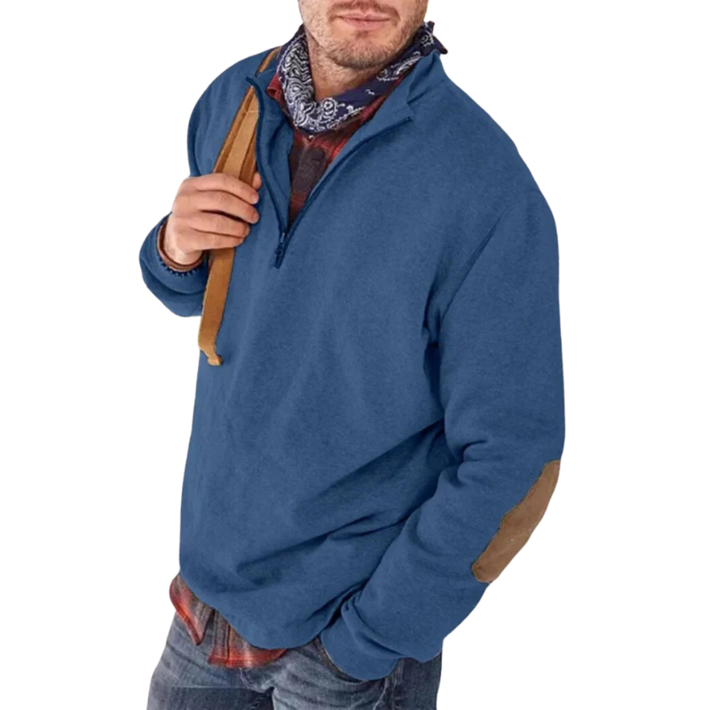 Mand iført blå trøje med lynlås, brune albuelapper og ternet skjorte. Casual herremode, efterårsbeklædning, stilfuldt og komfortabelt look.