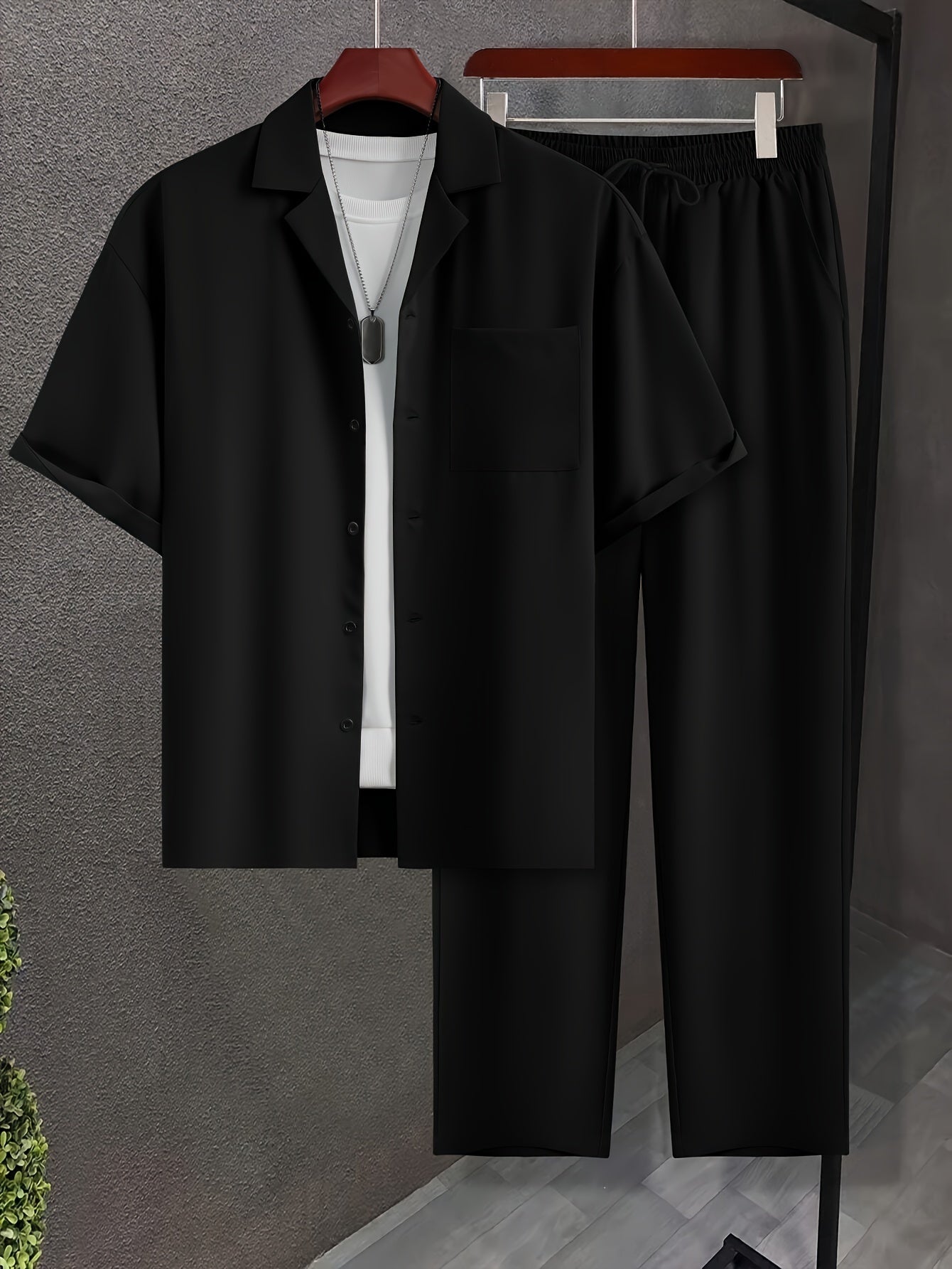 Sort herresæt med kortærmet skjorte og bukser, hængende på bøjler. Moderne herretøj, minimalistisk design, perfekt til casual eller formelle anledninger.