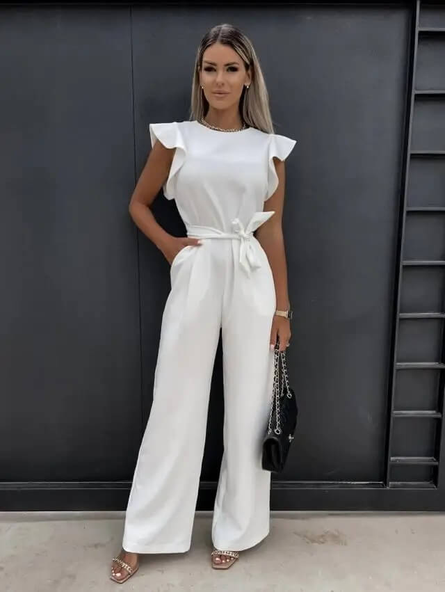 Kvinde i elegant hvid buksedragt med bælte, poserer foran sort baggrund. Mode, stilfuldt outfit, moderne kvindetøj, sommerlook.