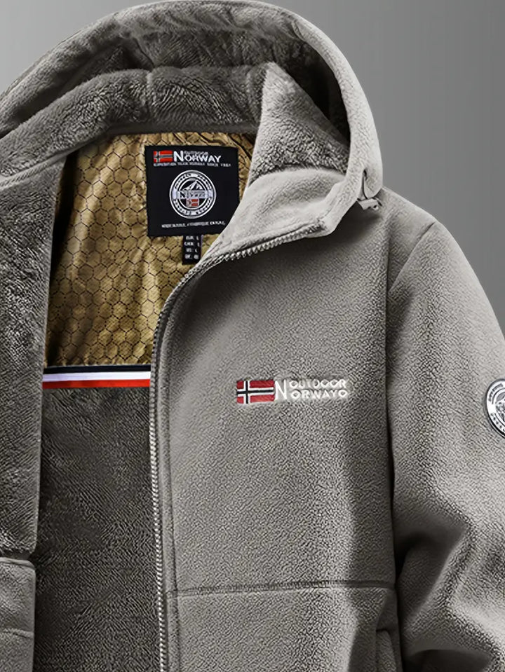 Grå softshell jakke med hætte, norsk flag og Outdoor Norway logo. Varm fleeceforing, velegnet til udendørs aktiviteter. Ideel til koldt vejr.