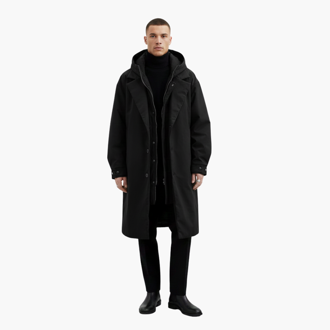 Mand iført sort frakke, sort rullekrave og sorte bukser. Står mod hvid baggrund. Mode, herretøj, vinterjakke, minimalistisk stil.