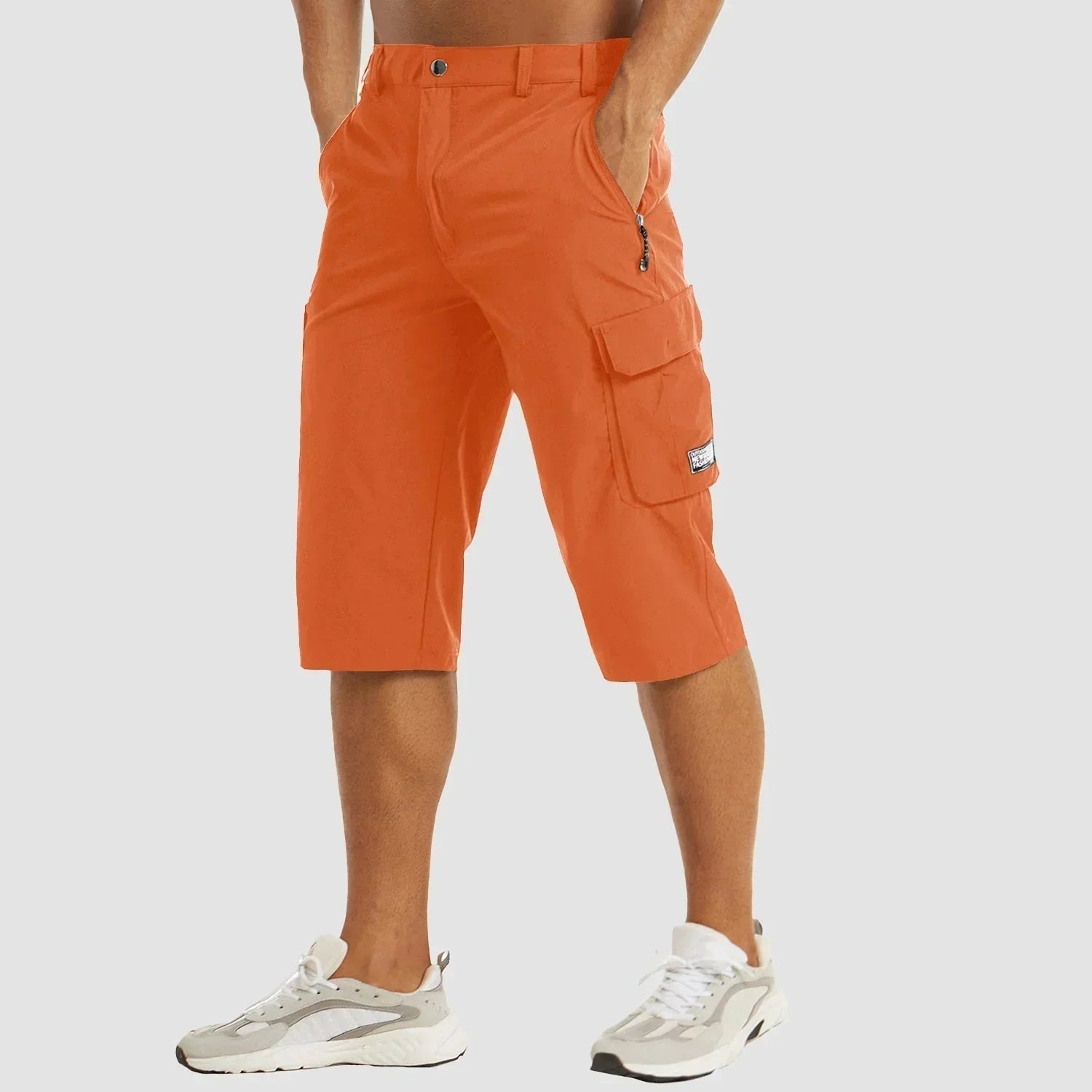 Mand iført orange cargoshorts med sidelommer og hvide sneakers. Moderne herremode, sommeroutfit, praktiske shorts til udendørs aktiviteter.