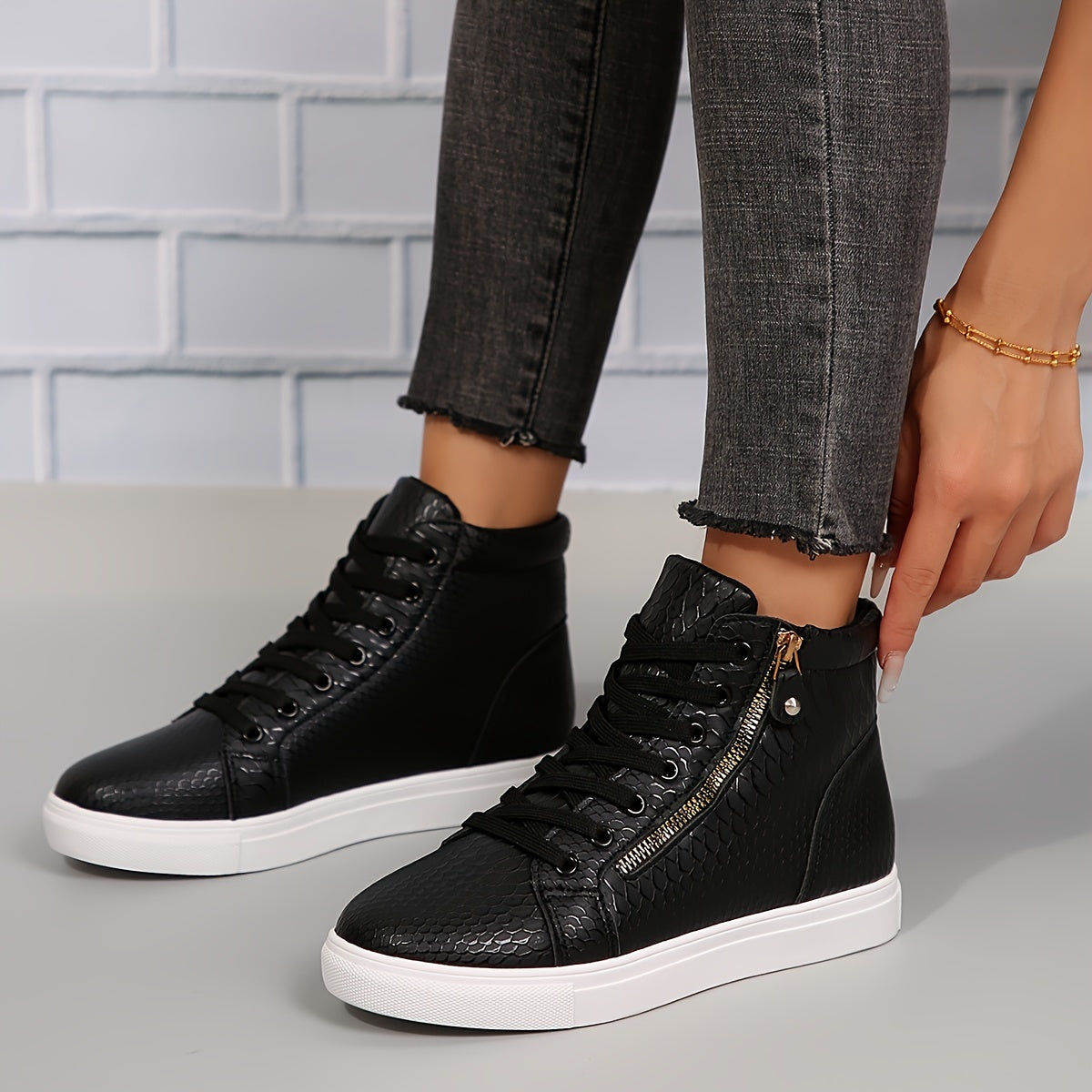 Kvinde iført sorte højtop sneakers med hvid sål og lynlåsdetalje, justerer skoen. Moderne mode, casual stil, trendy fodtøj.