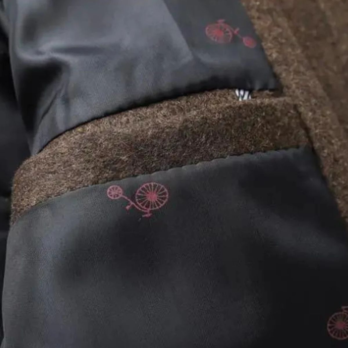 Brun uldfrakke med sort foring og røde cykelmotiver. Elegant herrejakke, vintermode, stilfuldt design, kvalitetsmaterialer.