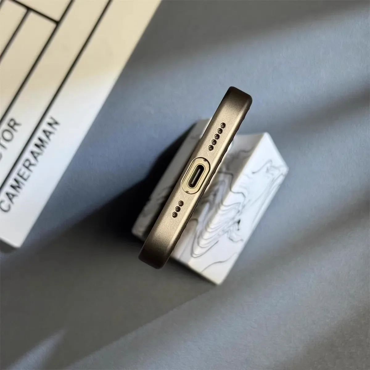 Smartphone i metalramme set fra bunden med USB-C port og højttalerhuller, placeret på marmorbord. Moderne teknologi, minimalistisk design.