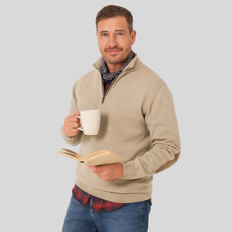 En mand i beige trøje holder en hvid kop og en åben bog. Han har et afslappet udtryk og står foran en grå baggrund.