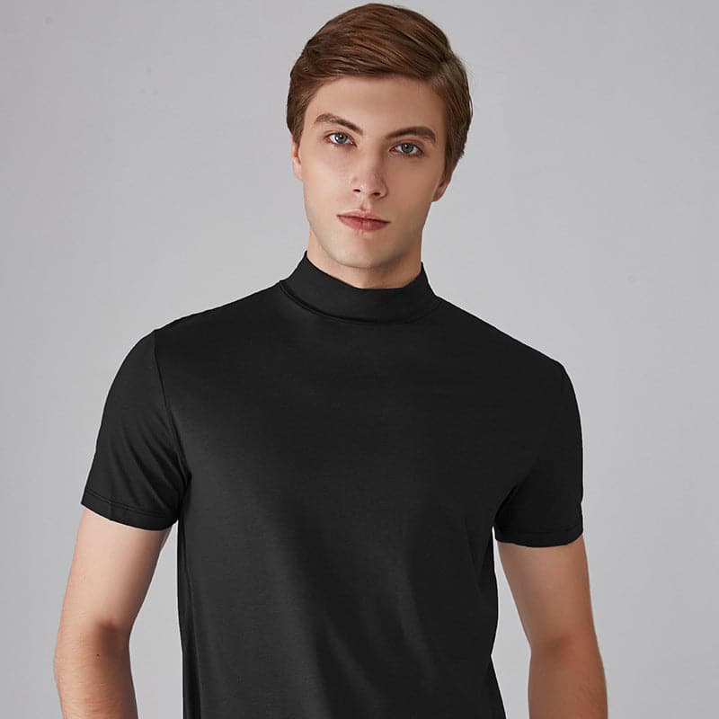 Ung mand iført sort t-shirt med høj hals, poserer mod grå baggrund. Moderne herremode, minimalistisk stil, casual tøj.