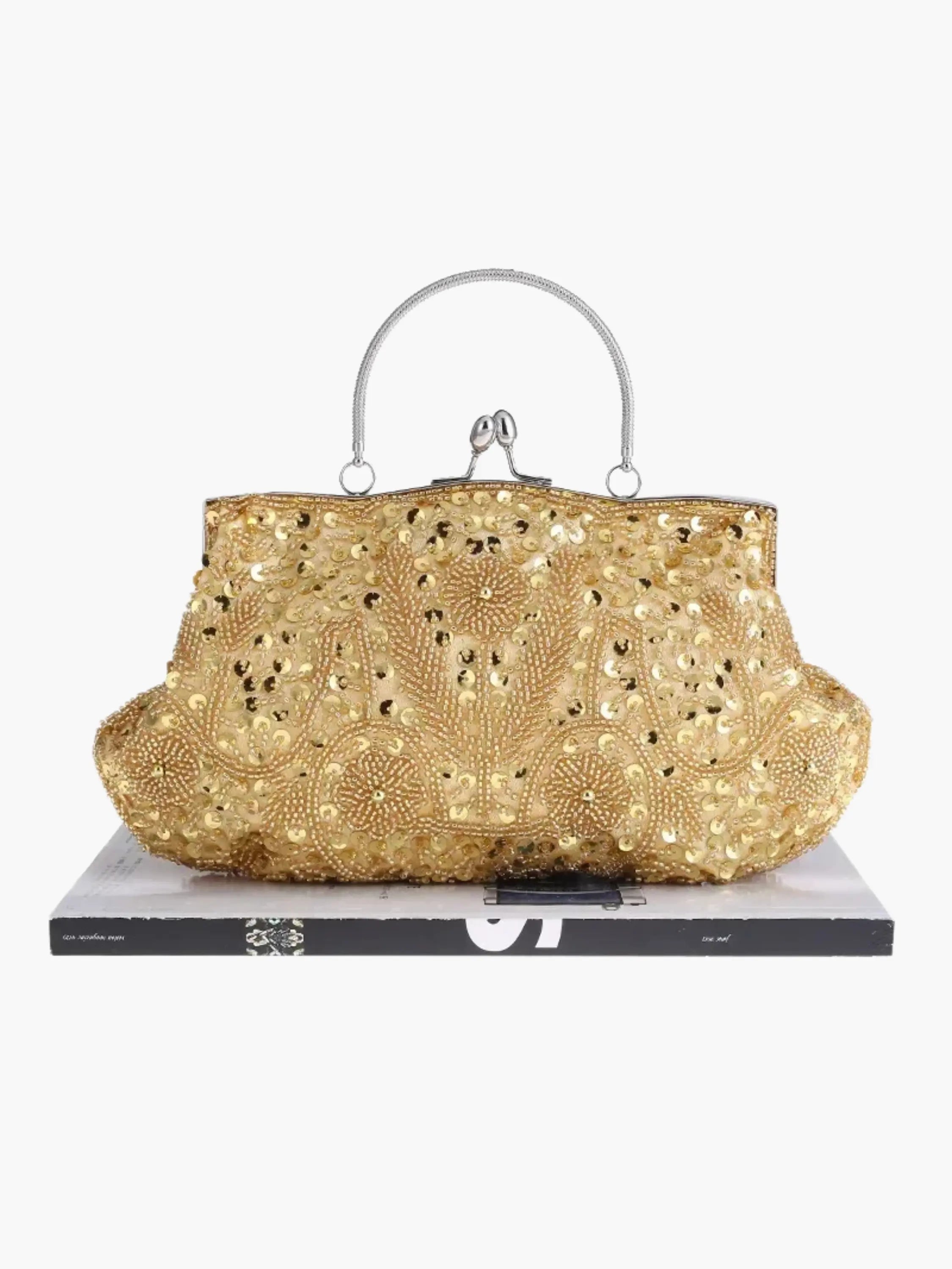 Guld vintage håndtaske med perlebroderi og metalhank, placeret på en bog. Elegant design, perfekt til festlige lejligheder.