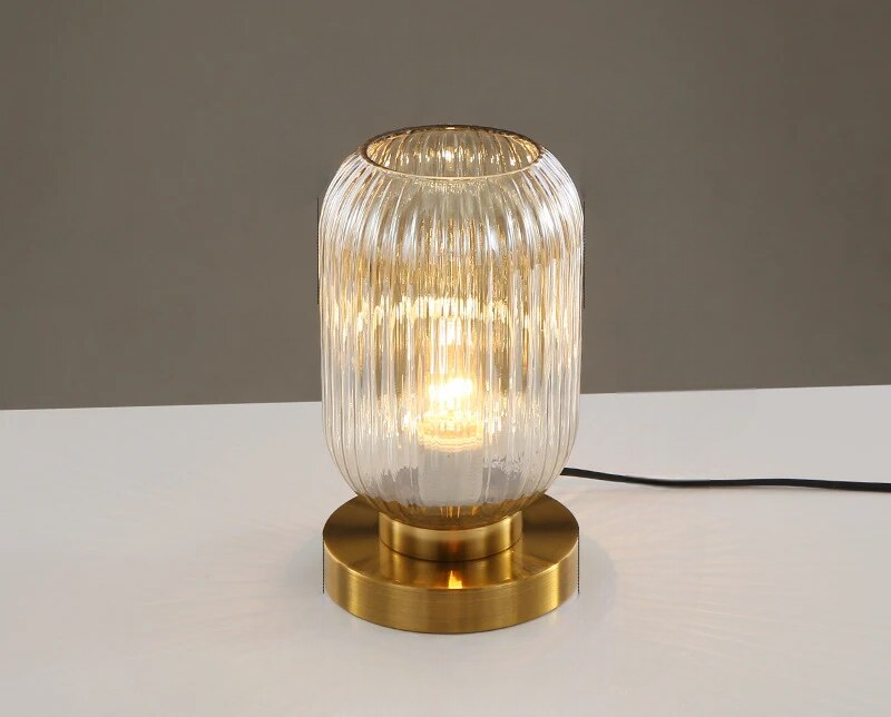 Ribbet glasbordlampe med gylden base, moderne design, tændt pære, stilfuld belysning til hjemmet, elegant interiørdekoration.
