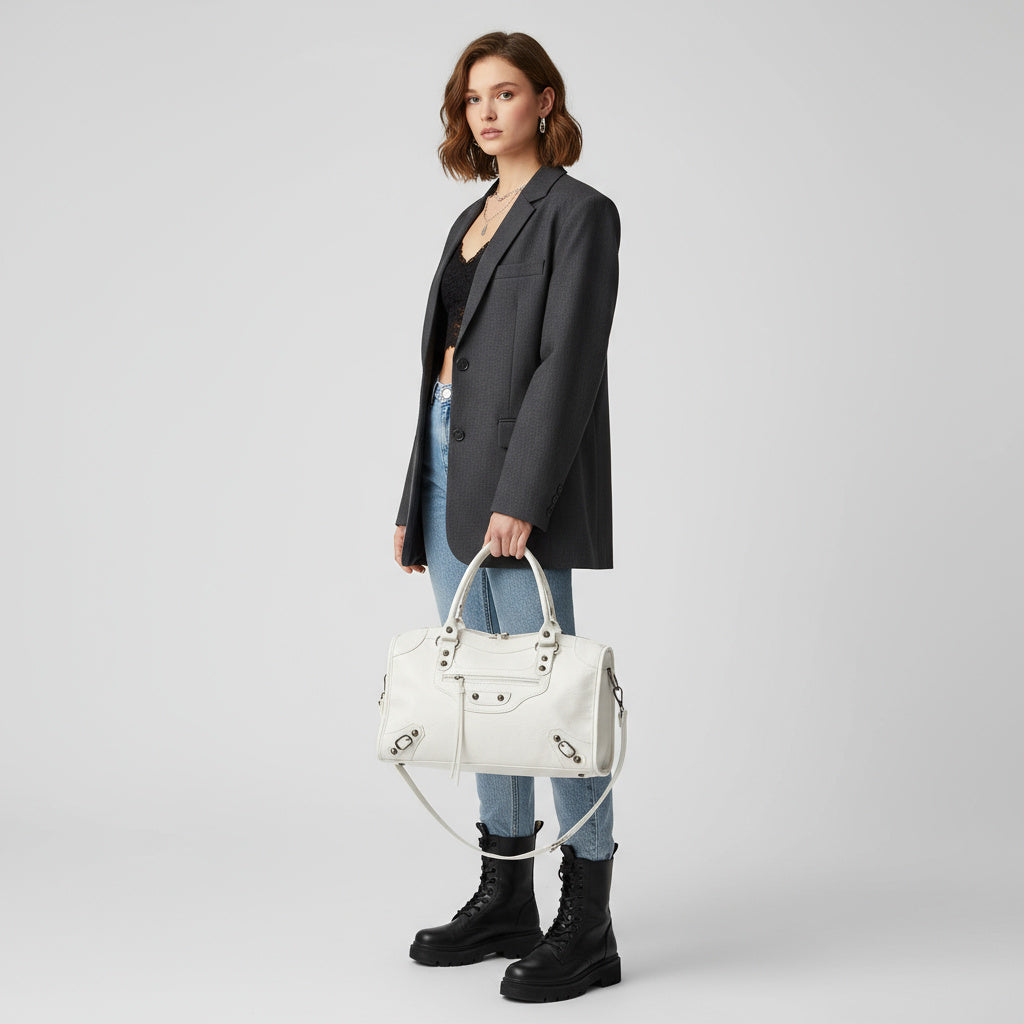 Ung kvinde i grå blazer og jeans, bærer en hvid designerhåndtaske og sorte støvler. Mode, stilfuldt outfit, moderne kvindetøj.