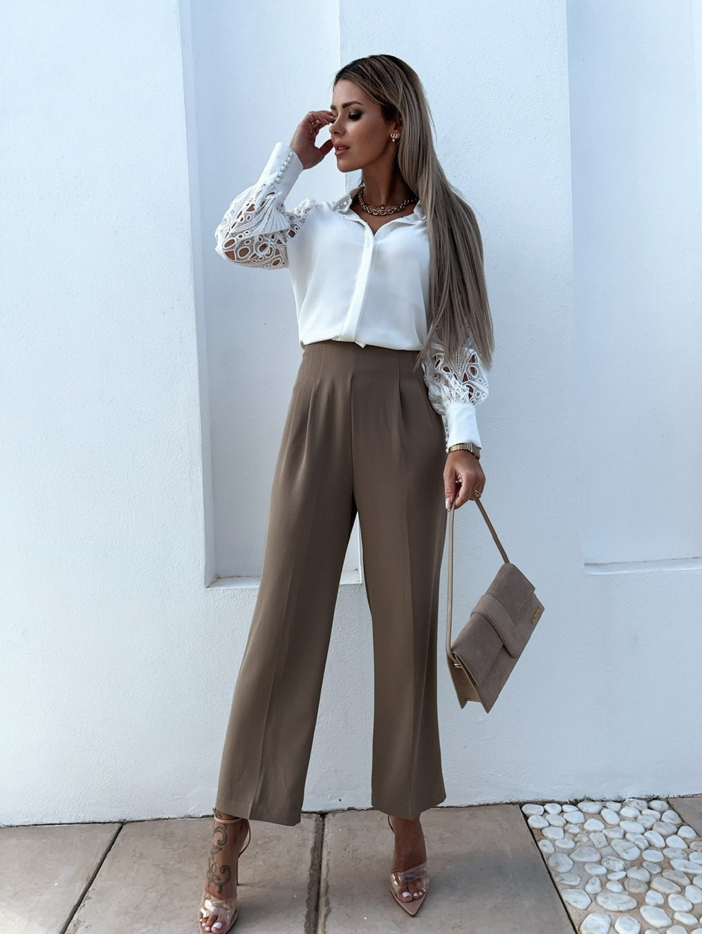 Kvinde i elegant outfit med hvid blondebluse og beige bukser, holder en beige taske. Perfekt til modeblog, stilfuldt tøj, moderne kvindemode.