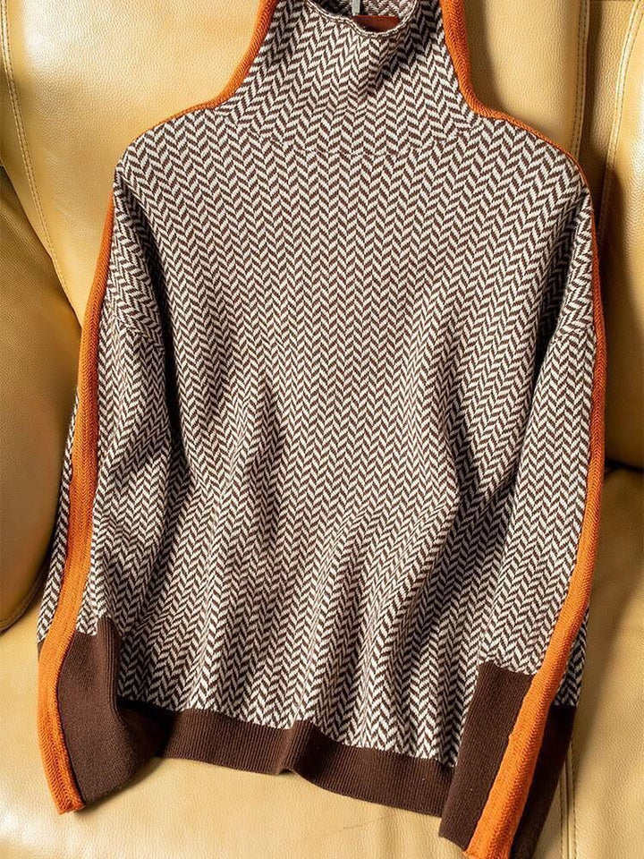 Brun og hvid striktrøje med zigzag-mønster og orange kanter, placeret på en læderstol. Moderne design, varm vintermode, komfortabel sweater.