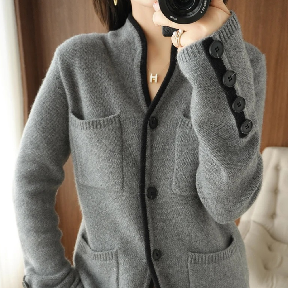 Kvinde iført grå cardigan med sorte knapper og lommer, fotograferet indendørs. Striktrøje, mode, vintertøj, stilfuldt design, komfortabel beklædning.