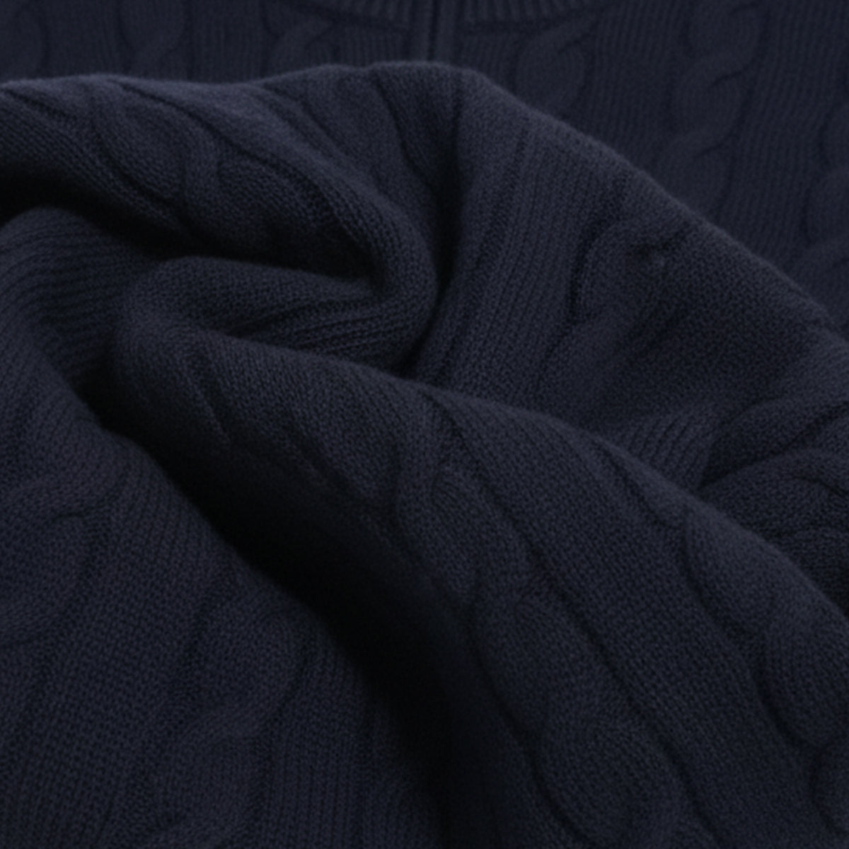 Mørkeblå kabelstrik trøje i uld, tæt på. Blød tekstur, klassisk design, perfekt til vintermode. Komfortabel og stilfuld beklædning.