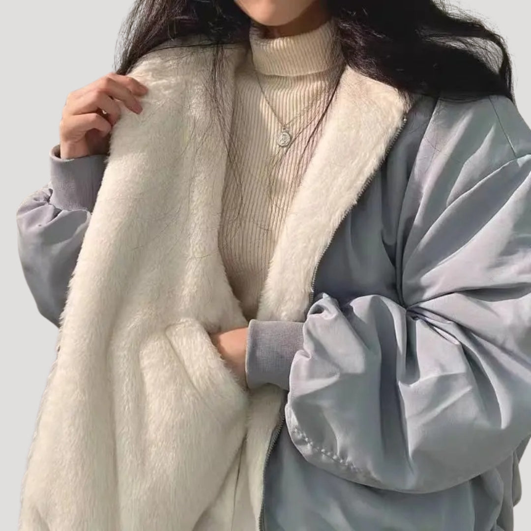 Kvinde iført grå jakke med hvidt plysfor, beige striktrøje og halskæde. Vintermode, stilfuld overtøj, trendy damejakke.