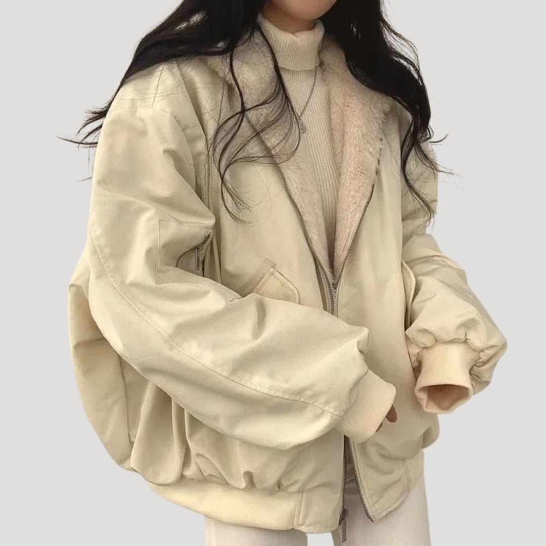 Kvinde iført beige oversized bomberjakke med pelskrave og lynlås, kombineret med lys sweater. Trendy vintermode, casual stil.